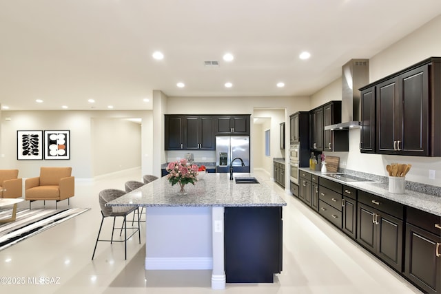 13711 N Hidden Springs Dr, Oro Valley, AZ 85755 - kitchen with wall chimney exhaust hood, appliances with stainless steel finishes, a breakfast bar area, a spacious island, and light stone countertops