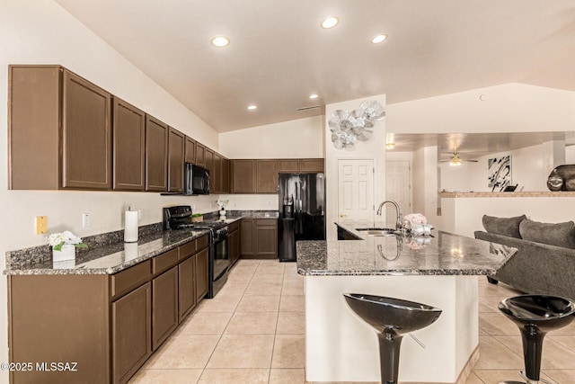 kitchen with dark stone counters, vaulted ceiling, a sink, black appliances, and light tile patterned floors