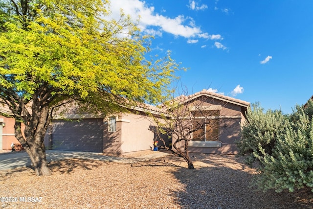 view of property hidden behind natural elements with a garage, a tile roof, dirt driveway, and stucco siding