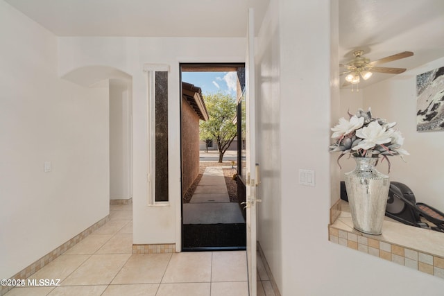doorway featuring arched walkways, baseboards, ceiling fan, and light tile patterned floors
