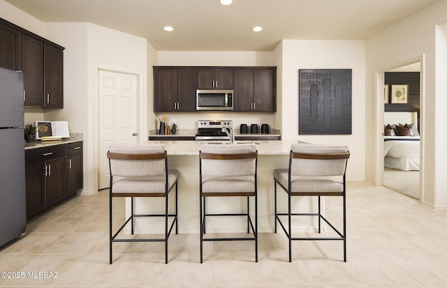 kitchen featuring light stone countertops, dark brown cabinets, a breakfast bar area, recessed lighting, and stainless steel appliances