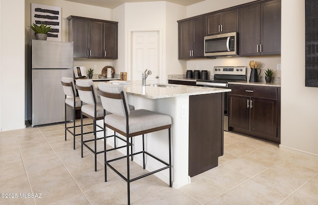 kitchen with dark brown cabinets, a breakfast bar, a sink, appliances with stainless steel finishes, and light tile patterned floors