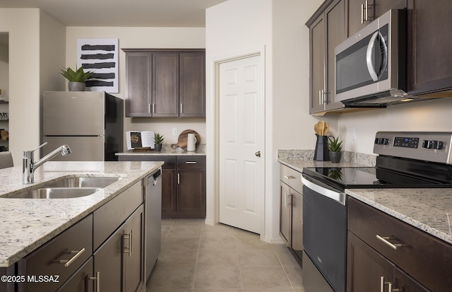 kitchen with a sink, light tile patterned floors, dark brown cabinets, and stainless steel appliances