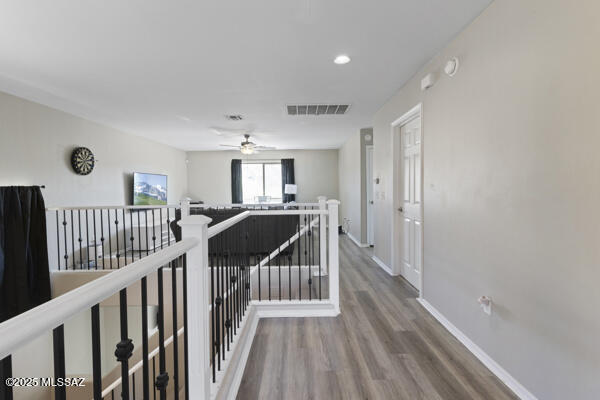 hall featuring visible vents, wood finished floors, baseboards, recessed lighting, and an upstairs landing