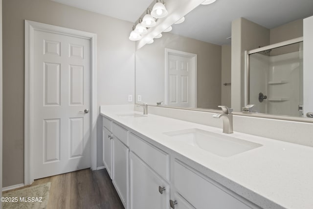 bathroom with a sink, double vanity, an enclosed shower, and wood finished floors