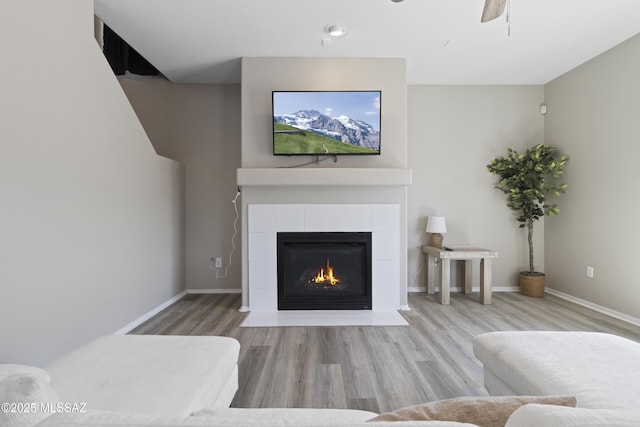 living area featuring baseboards, a fireplace, a ceiling fan, and wood finished floors