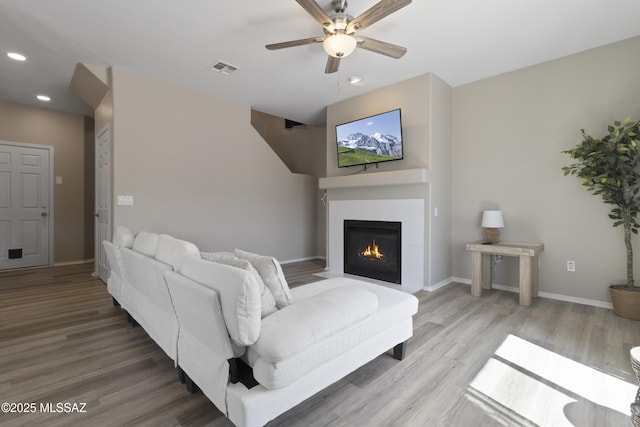 living room featuring ceiling fan, visible vents, wood finished floors, a glass covered fireplace, and recessed lighting
