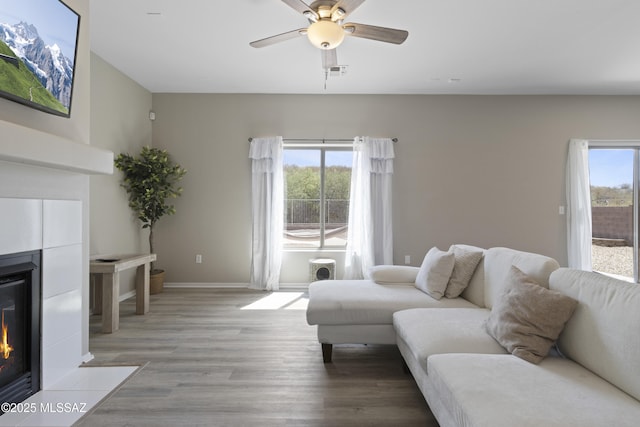 living room with a ceiling fan, baseboards, a tiled fireplace, and light wood-style flooring