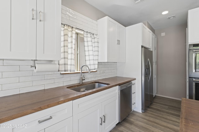 kitchen with appliances with stainless steel finishes, a sink, wooden counters, decorative backsplash, and dark wood-type flooring