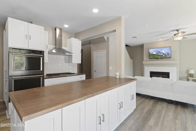 kitchen featuring a glass covered fireplace, wall chimney exhaust hood, stainless steel appliances, open floor plan, and backsplash