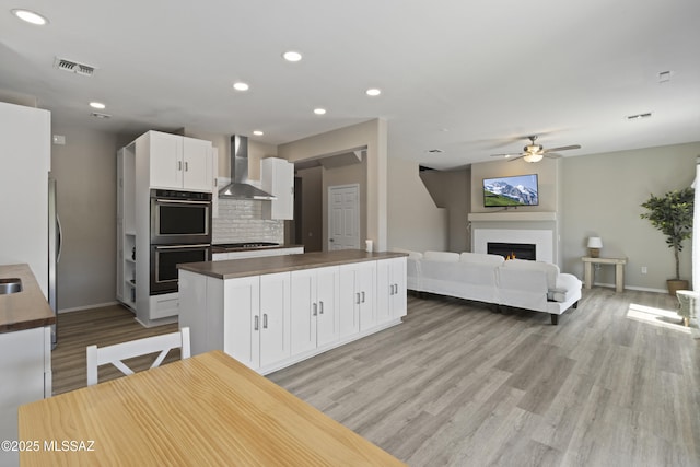 kitchen featuring multiple ovens, wooden counters, visible vents, and wall chimney range hood