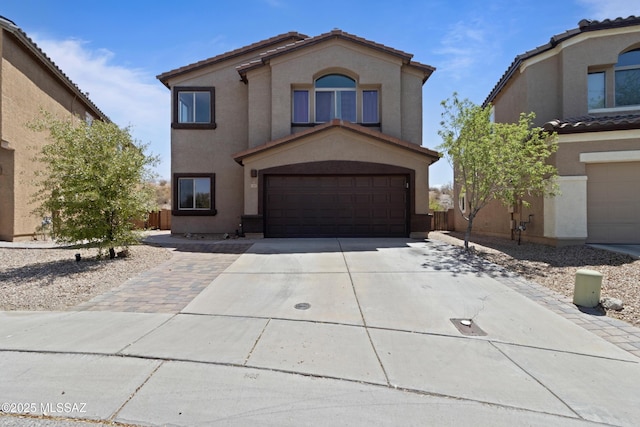 mediterranean / spanish-style home with a garage, stucco siding, a tiled roof, and concrete driveway