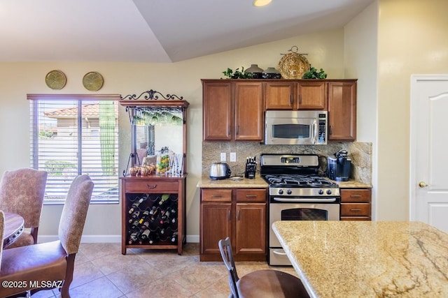 61867 E Ironwood Ln, Tucson, AZ 85739 - kitchen with light tile patterned flooring, brown cabinets, tasteful backsplash, vaulted ceiling, and stainless steel appliances