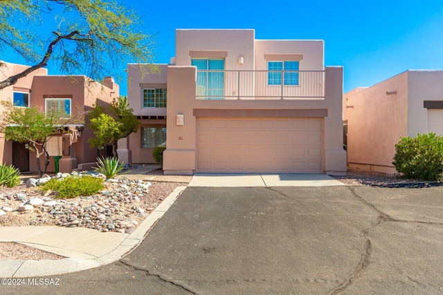 adobe home with an attached garage, aphalt driveway, stucco siding, and a balcony