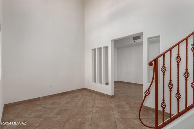 empty room featuring tile patterned floors, a high ceiling, baseboards, and visible vents