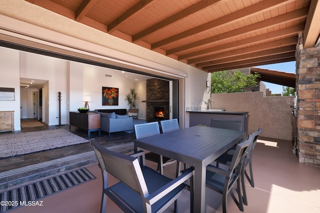 view of patio / terrace with exterior kitchen, a sink, and a warm lit fireplace