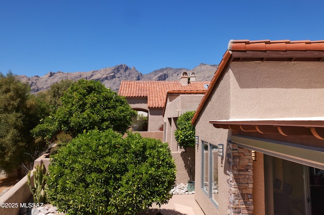 view of home's exterior featuring stone siding, a tiled roof, a mountain view, and stucco siding