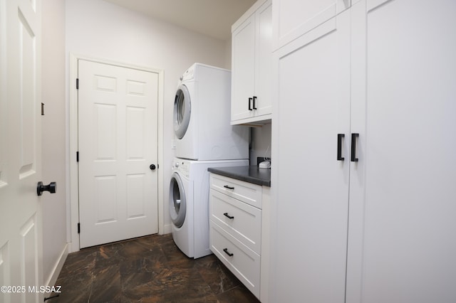 clothes washing area featuring cabinet space, baseboards, marble finish floor, and stacked washer / dryer