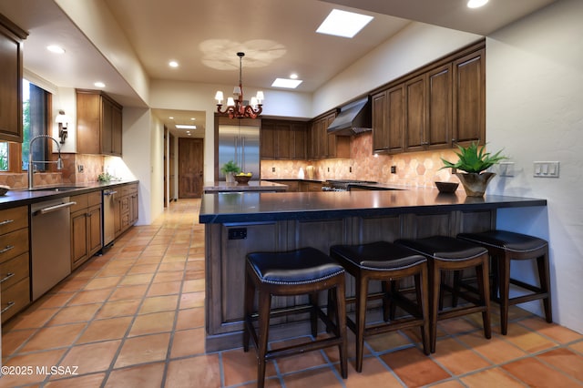 4915 N Via De La Granja, Tucson, AZ 85718 - kitchen featuring wall chimney exhaust hood, stainless steel appliances, a sink, dark countertops, and decorative backsplash