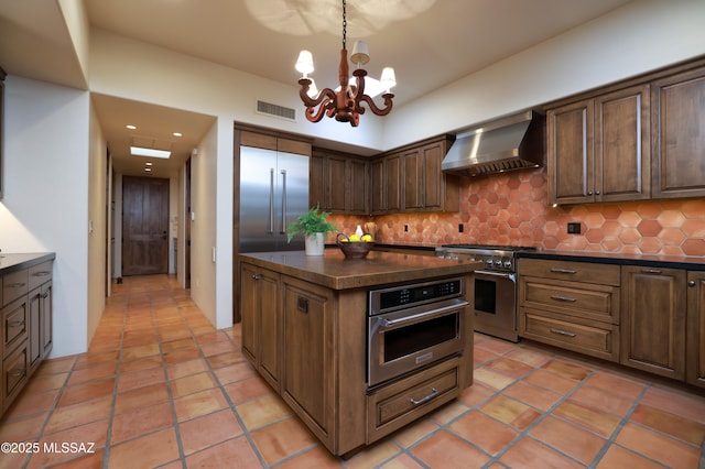 4915 N Via De La Granja, Tucson, AZ 85718 - kitchen featuring wall chimney exhaust hood, appliances with stainless steel finishes, dark countertops, tasteful backsplash, and a chandelier