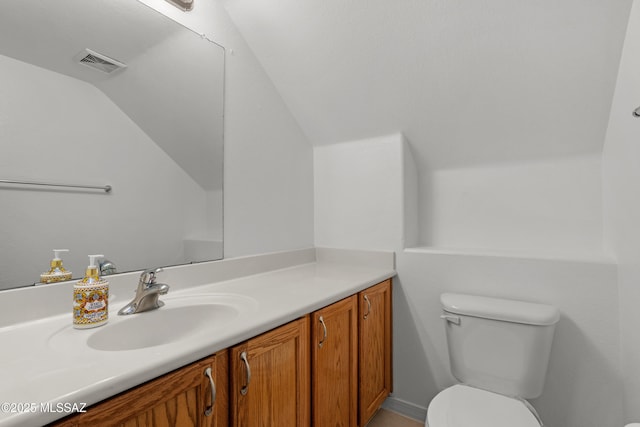 bathroom with visible vents, toilet, vanity, and vaulted ceiling