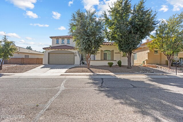 mediterranean / spanish-style house with a garage, concrete driveway, a tile roof, fence, and stucco siding