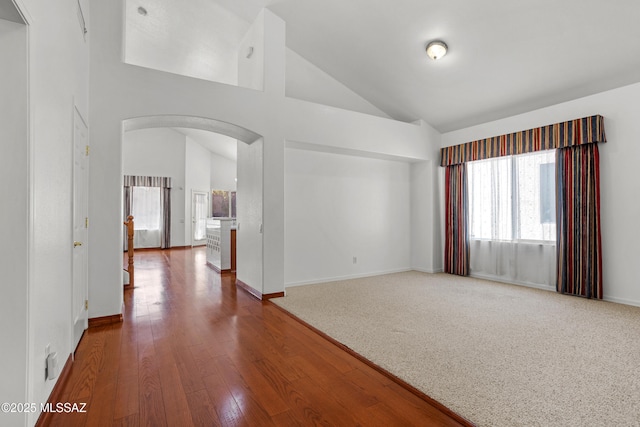 spare room featuring arched walkways, wood finished floors, high vaulted ceiling, and baseboards