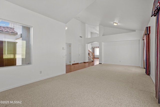 unfurnished living room with a wealth of natural light, arched walkways, high vaulted ceiling, and carpet floors