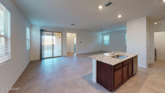 kitchen with stainless steel dishwasher, light stone countertops, a kitchen island with sink, a sink, and open floor plan