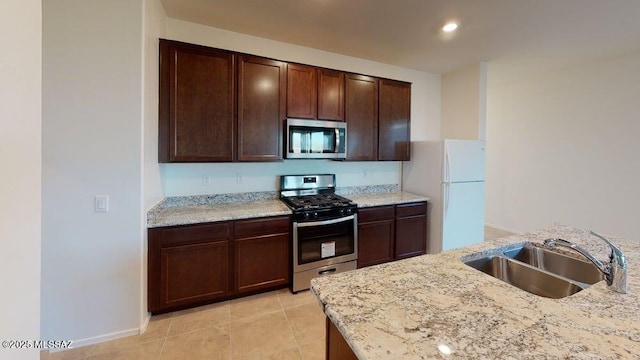 kitchen with a sink, dark brown cabinets, appliances with stainless steel finishes, and light stone counters