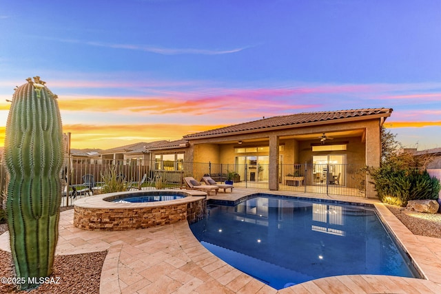 pool at dusk with fence, a patio area, and a pool with connected hot tub