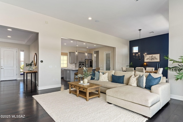 living area with baseboards, a notable chandelier, dark wood-type flooring, and recessed lighting