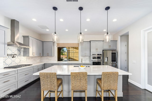 kitchen with wall chimney exhaust hood, a sink, backsplash, gray cabinets, and appliances with stainless steel finishes