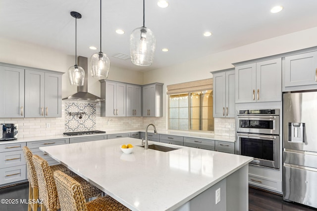 kitchen with a kitchen breakfast bar, wall chimney range hood, a sink, gray cabinetry, and appliances with stainless steel finishes