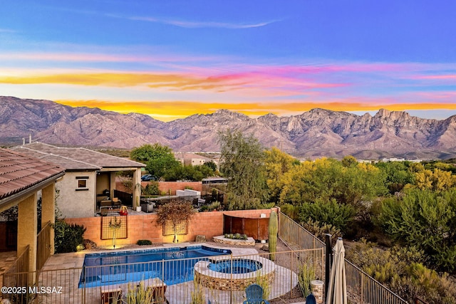 view of pool featuring a patio area, a fenced backyard, a pool with connected hot tub, and a mountain view
