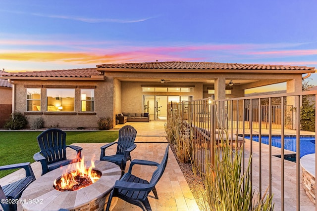 back of property at dusk featuring a patio area, ceiling fan, a yard, an outdoor pool, and stucco siding