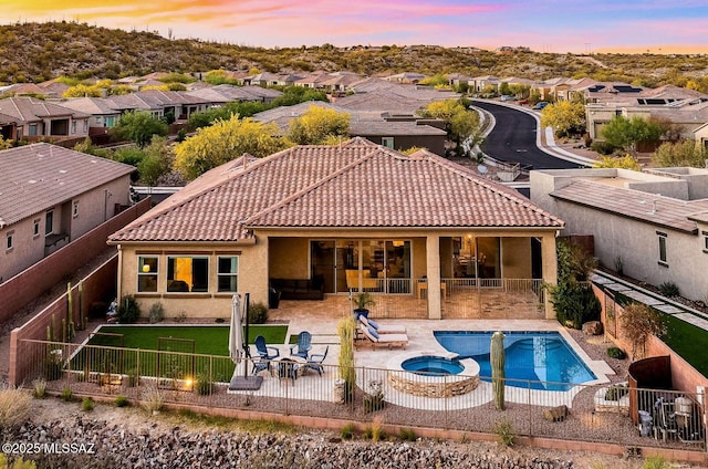 back of house at dusk with a residential view, a pool with connected hot tub, a patio, and a fenced backyard
