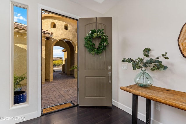 foyer featuring arched walkways, dark wood-type flooring, and baseboards