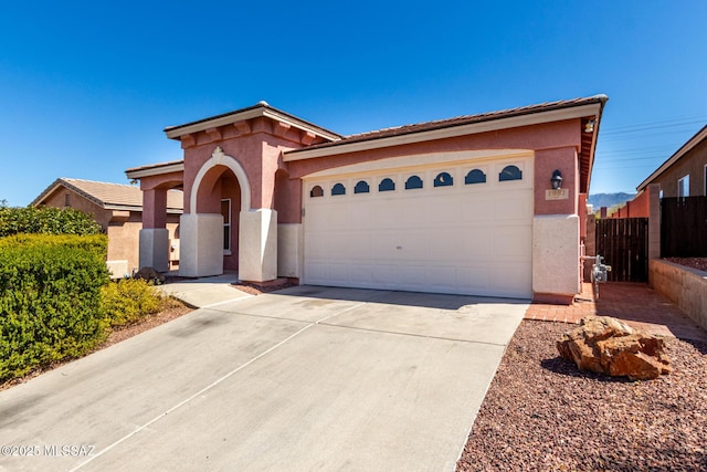 mediterranean / spanish-style home with an attached garage, driveway, stucco siding, and fence