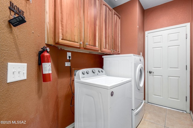 laundry room with a textured wall, cabinet space, washing machine and dryer, and light tile patterned floors