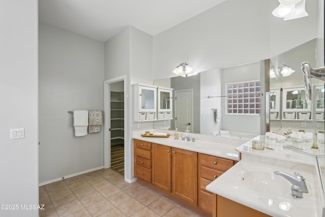 bathroom with two vanities, baseboards, tile patterned flooring, a walk in closet, and a sink
