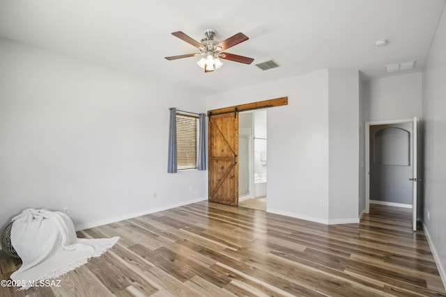 unfurnished bedroom featuring light wood finished floors, baseboards, visible vents, and a barn door