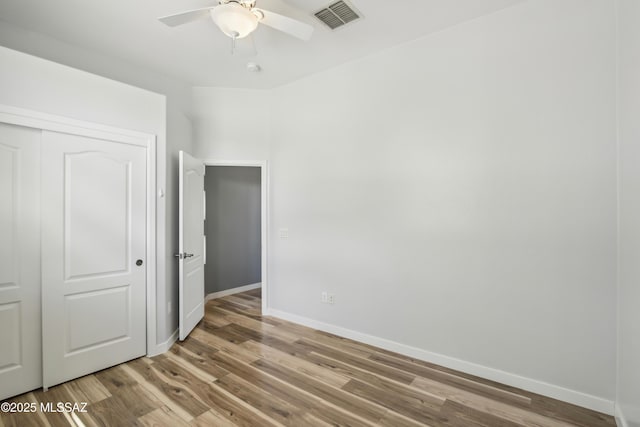 unfurnished bedroom featuring a closet, baseboards, visible vents, ceiling fan, and wood finished floors