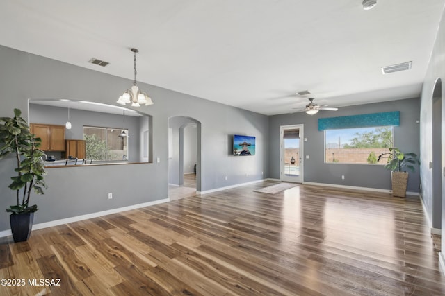 unfurnished living room with arched walkways, wood finished floors, visible vents, and ceiling fan with notable chandelier