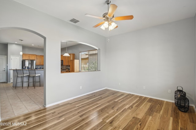 unfurnished room with arched walkways, light wood-style flooring, visible vents, and a ceiling fan