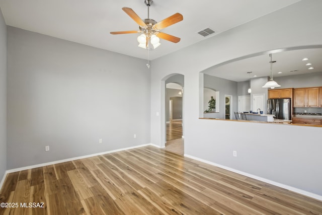 unfurnished living room with arched walkways, light wood-style flooring, visible vents, and ceiling fan