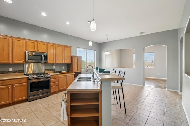kitchen featuring brown cabinetry, a sink, a kitchen bar, and appliances with stainless steel finishes