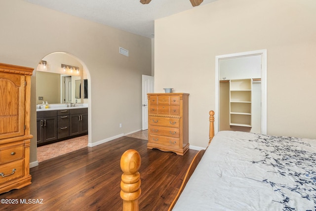 bedroom featuring arched walkways, ensuite bath, a closet, dark wood-style flooring, and visible vents
