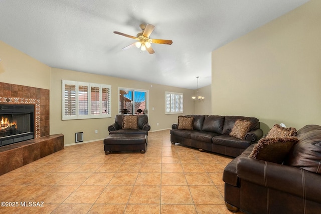 living area with a tile fireplace, baseboards, vaulted ceiling, and ceiling fan with notable chandelier