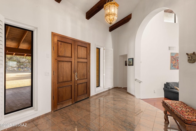 foyer with a high ceiling, visible vents, arched walkways, beamed ceiling, and baseboards